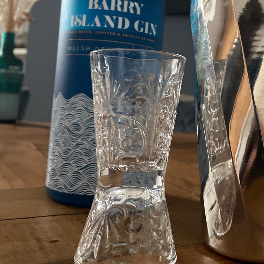 Italian Cut Glass jigger with single and double measure for making cocktails next to a cocktail shaker and a bottle of Barry island Gin