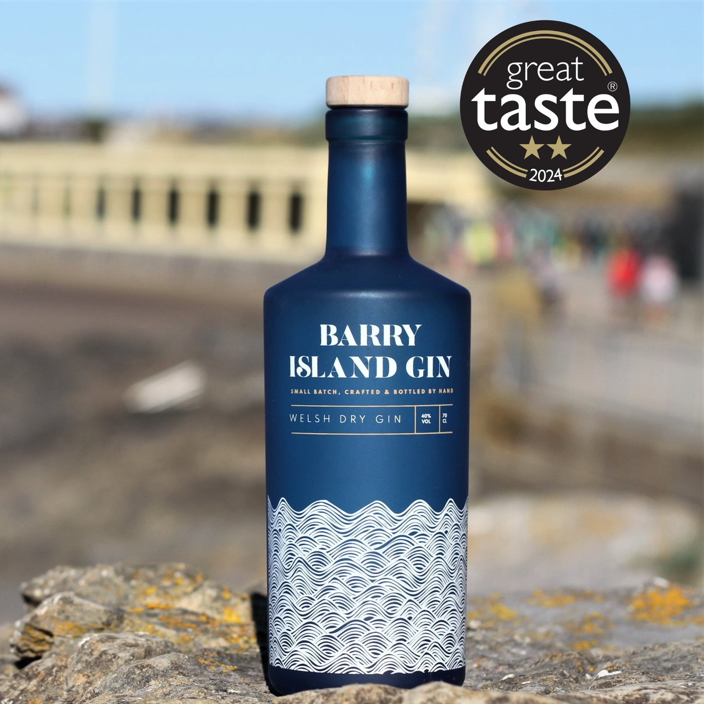 A bottle of Barry Island Welsh Dry Gin on Barry Island beach with a 2 star Great Taste Awards Logo 